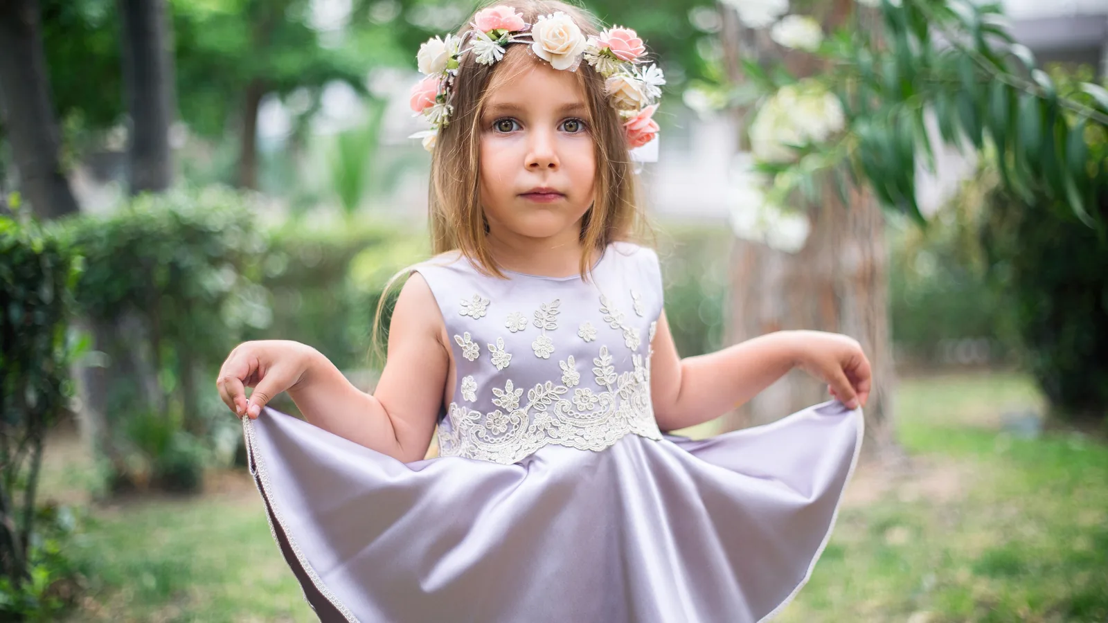 دختربچه‌ای با پیراهن یاسی پف‌دار و تاج گل در باغ